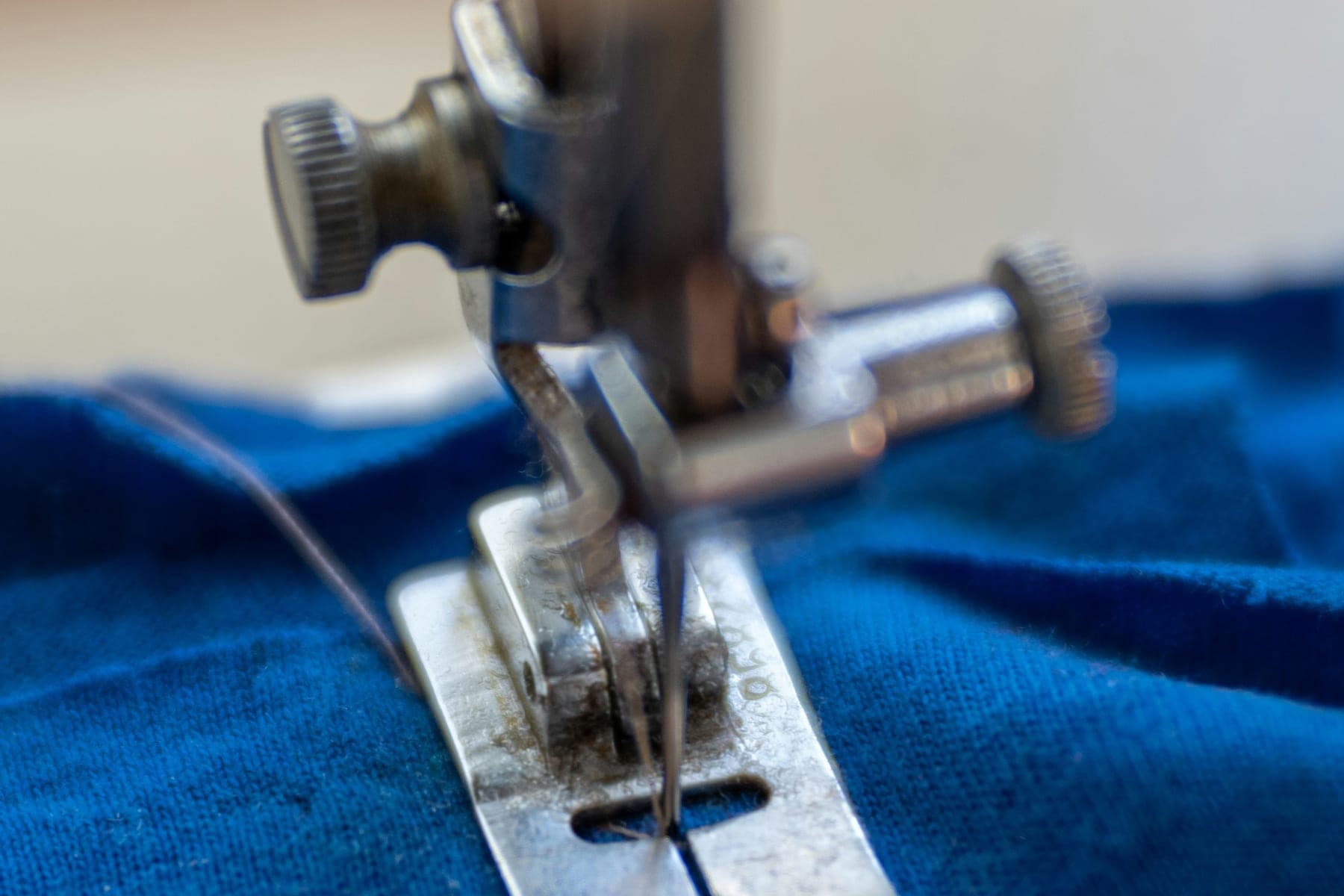 The presser foot and needle of a sewing machine on blue fabric
